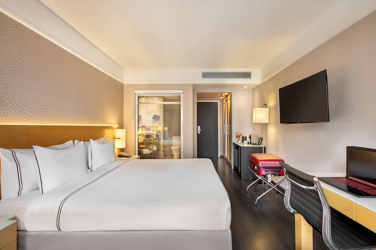Hotellihuone, jossa on suuri sänky, työpöytä kannettavalla tietokoneella, televisio ja matkalaukku.
