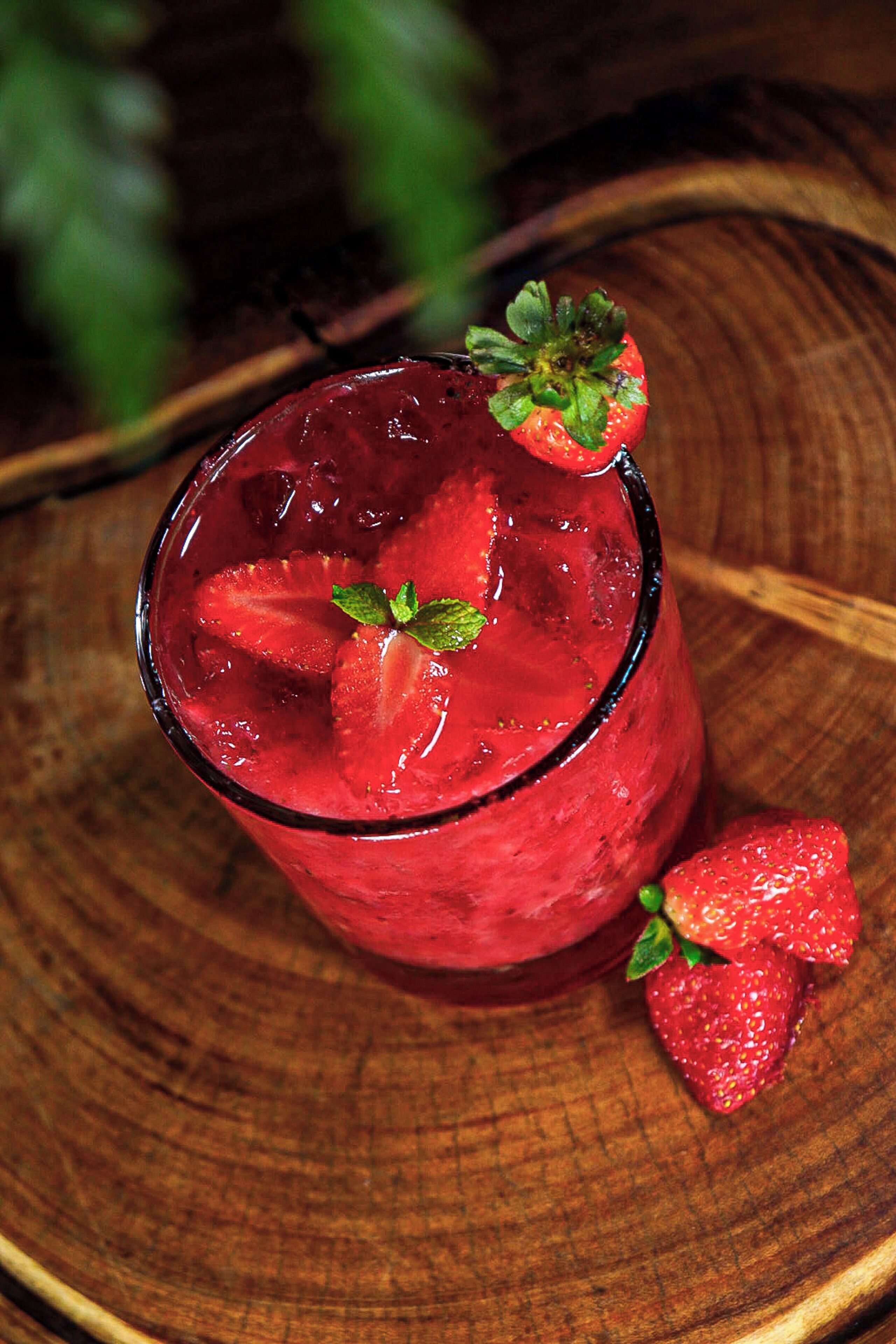 Un vaso de bebida roja con hielo y fresas sobre una superficie de madera.