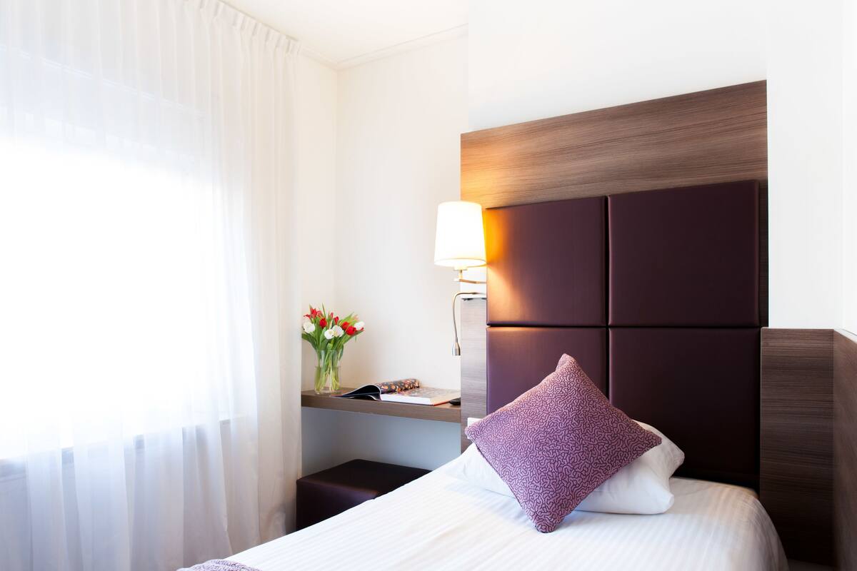 A hotel room with a bed, a nightstand, a lamp, and a window with curtains.