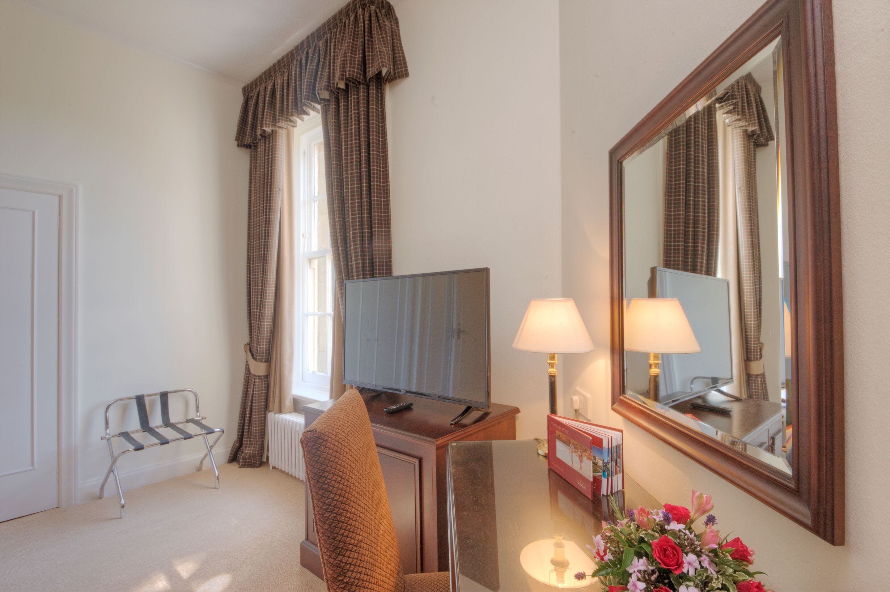 Une chambre d’hôtel équipée d’une télévision, de deux lampes, d’une chaise, d’une petite table et d’un miroir.