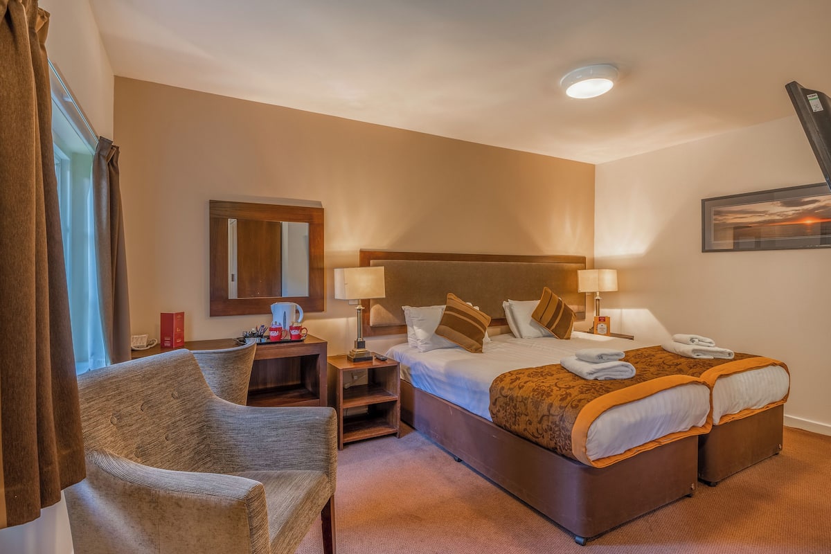 A hotel room with a large bed, two bedside tables, a chair, a desk, and a mirror.