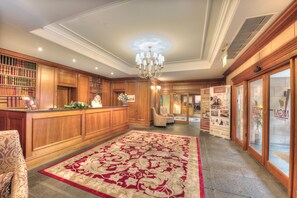 A reception area with a red and white carpet, wooden reception desk, and a chandelier.