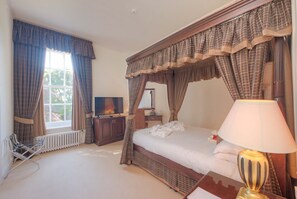 A bedroom with a four-poster bed, a bedside lamp, a flat-screen TV, a radiator, and a window with curtains. - Muthu Newton Hotel (Near Inverness Airport) (Nairn)