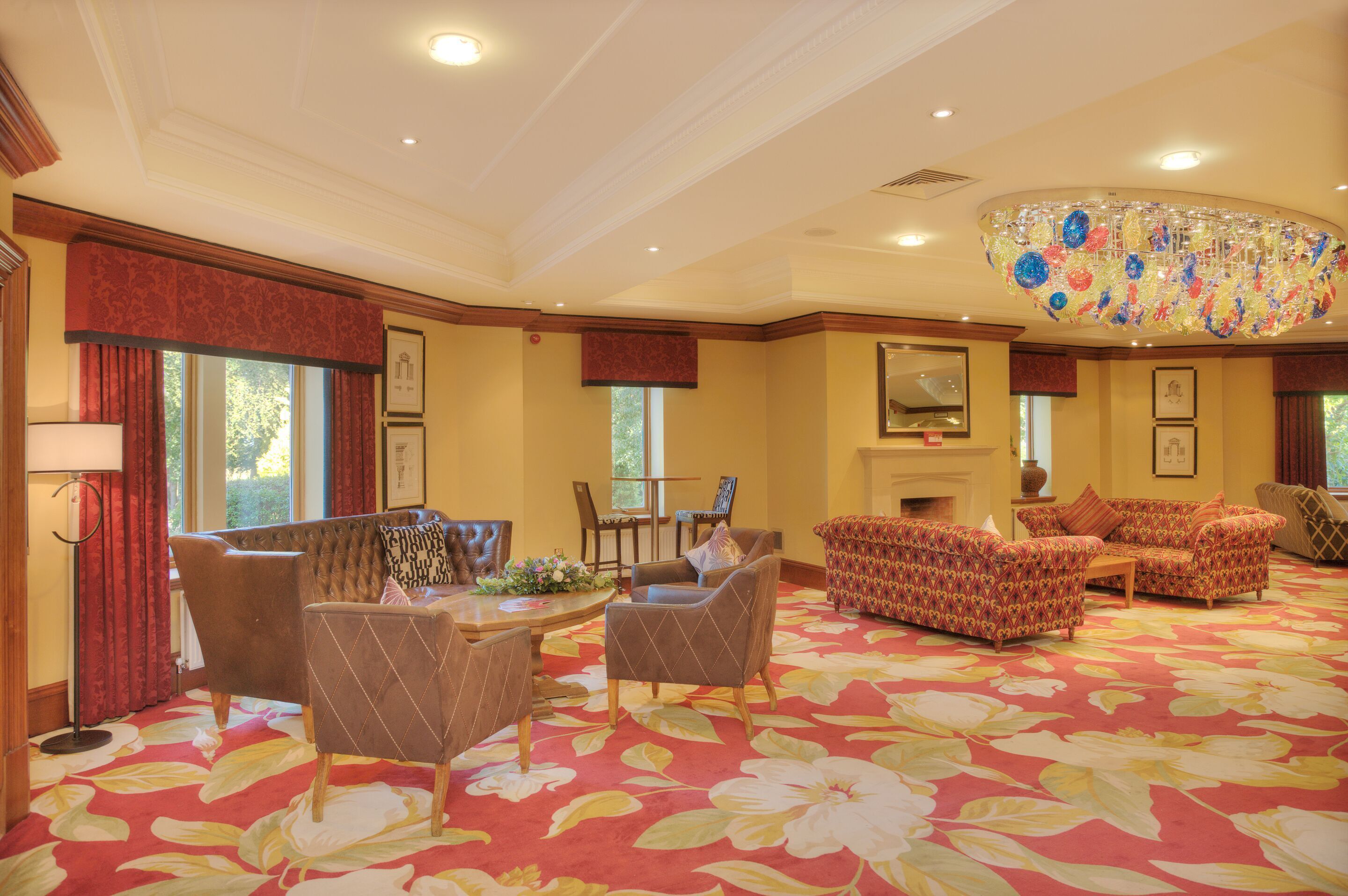 Een ruime woonkamer met een bloemenprint tapijt, een open haard en een grote kroonluchter.