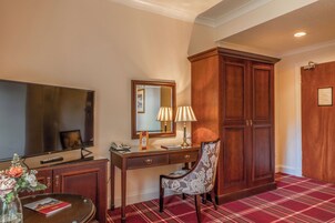 Habitación de hotel con un televisor de pantalla plana grande, un escritorio de madera con lámpara, una silla y un armario espacioso.