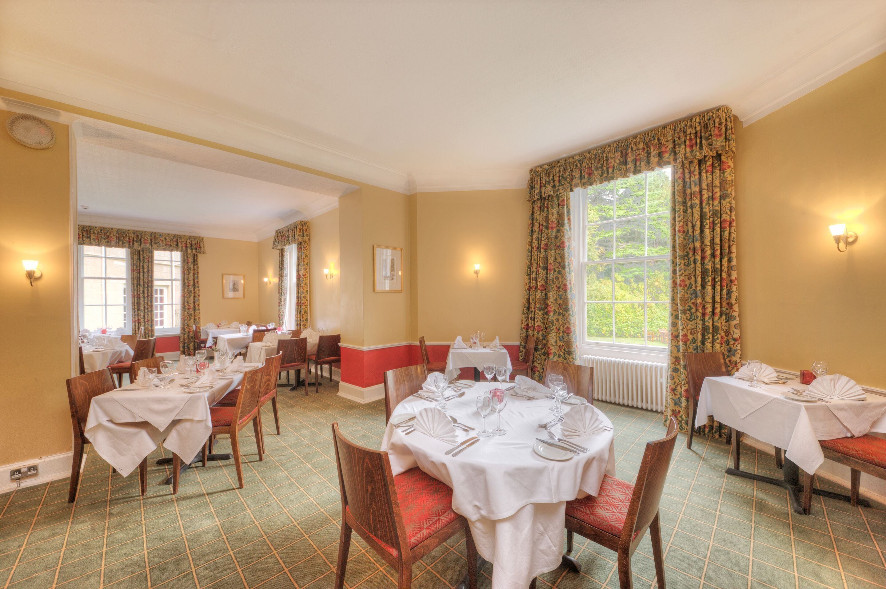 A dining area with multiple tables set for service, chairs, and a large window with curtains.
