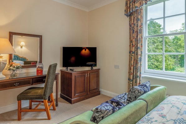 A hotel room with a wooden desk, a television on a cabinet, a green sofa, and a window with curtains. - Muthu Newton Hotel (Near Inverness Airport) (Nairn)