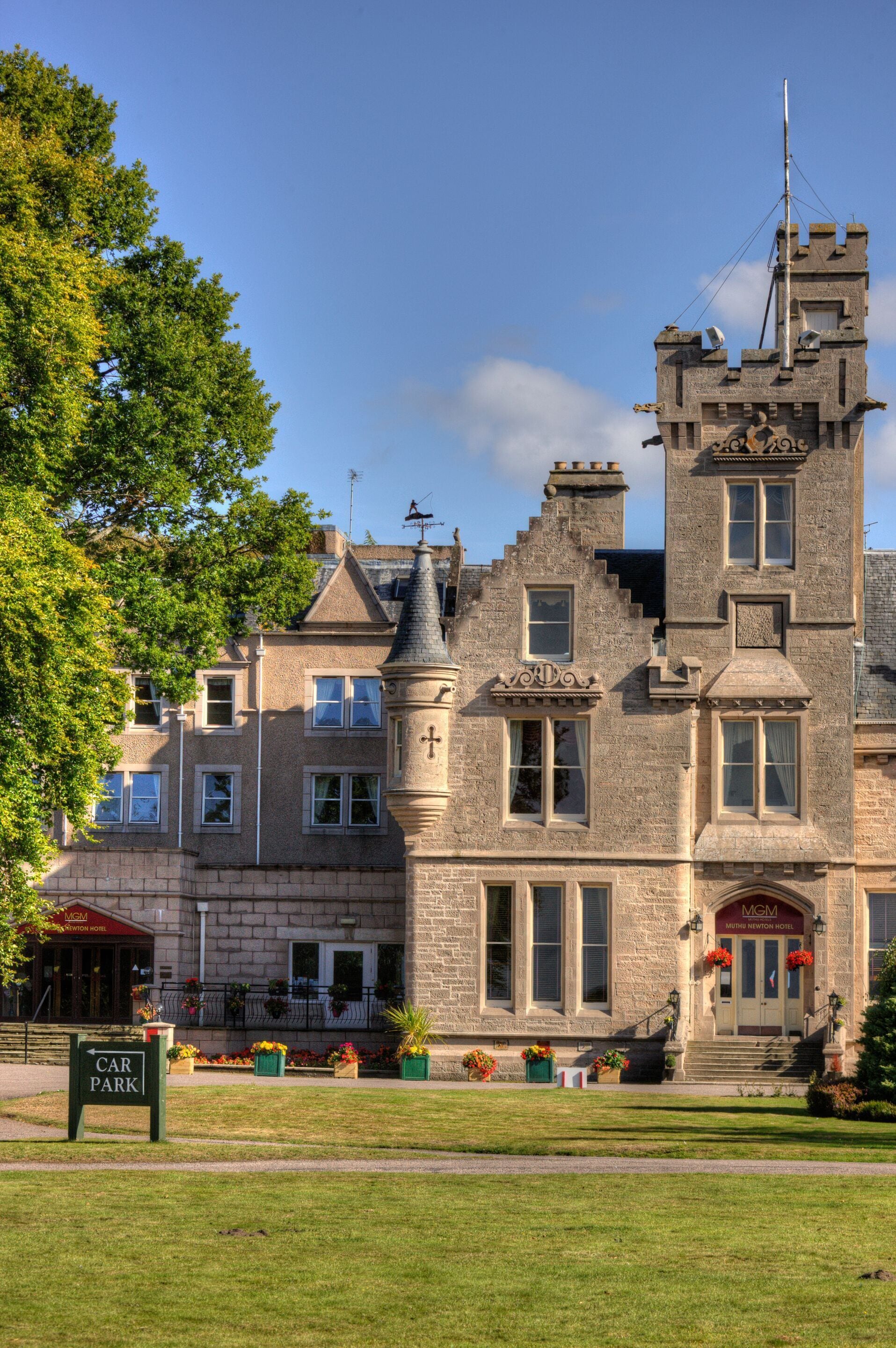 A historic stone building with a prominent tower, large windows, and a sign indicating a car park.