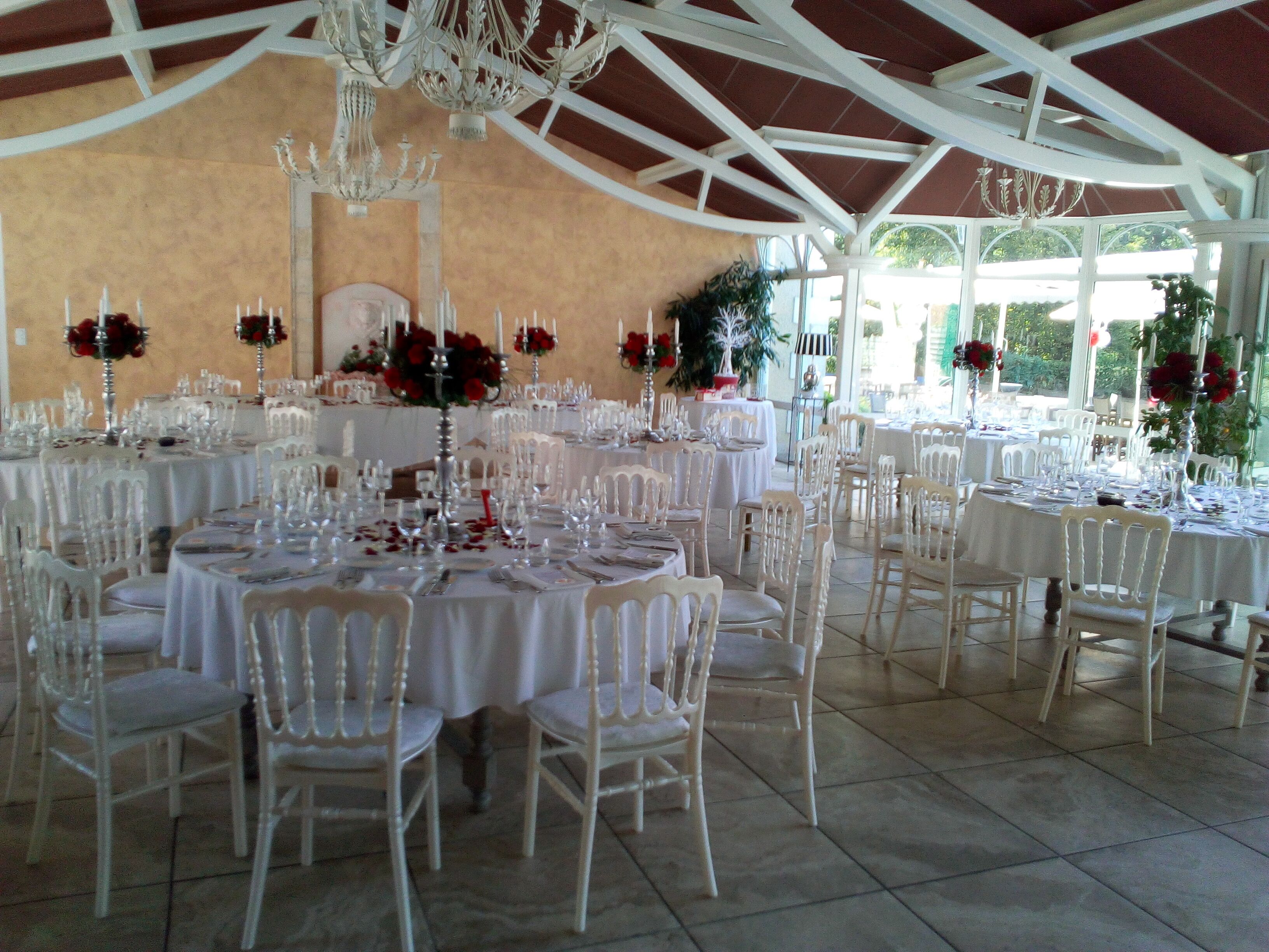 Un salón de banquetes con mesas redondas dispuestas para un evento formal, sillas blancas y candelabros.