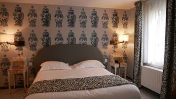 A bedroom with a large bed, two bedside tables with lamps, a patterned bedspread, and a wall with a repeating pattern of vases.