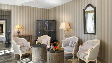 A room with striped wallpaper, two armchairs, a small table with a lamp, and a large mirror on the wall.