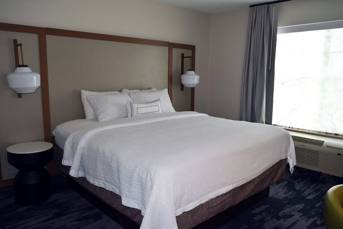 A hotel room with a large bed, two bedside lamps, a window with curtains, and a small round table.