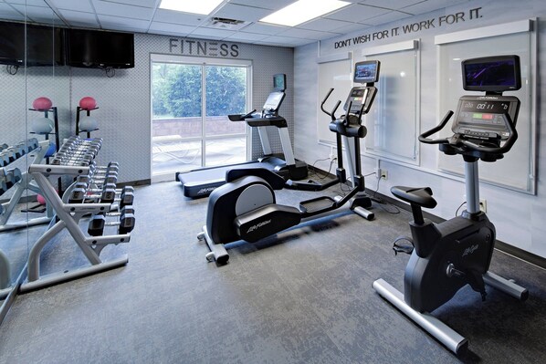 A gym with treadmills, elliptical machines, and dumbbells.