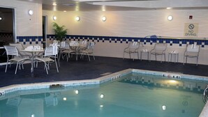 Un área de piscina interior con pared de azulejos, un cartel de 'No Diving' y varios conjuntos de asientos.