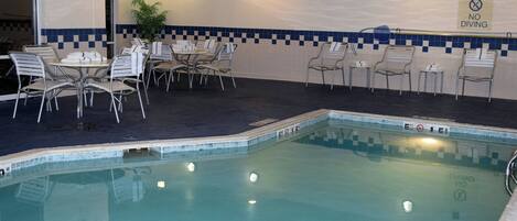 Un espace piscine intérieure avec un mur carrelé, un panneau indiquant « Il est interdit de plonger » et plusieurs types d’aménagements pour s’asseoir.