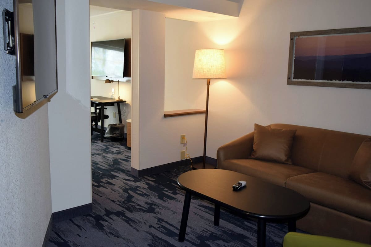 A hotel room with a brown sofa, a small table, a lamp, and a painting on the wall.