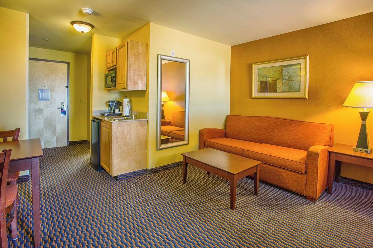 A compact hotel room with a kitchenette, a sofa, a coffee table, and a dining area.