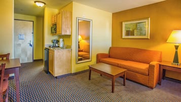 A compact hotel room with a kitchenette, a sofa, a coffee table, and a dining area.