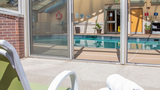 Uma área de piscina envidraçada com porta de vidro, uma cadeira verde e uma mesa com toalhas.