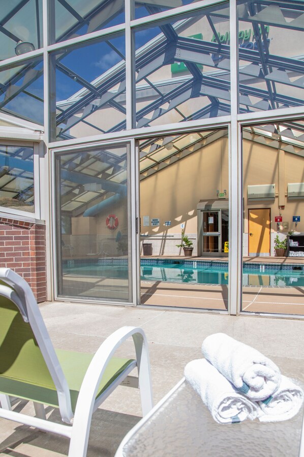 A glass-enclosed pool area with a glass door, a green chair, and a table with towels.
