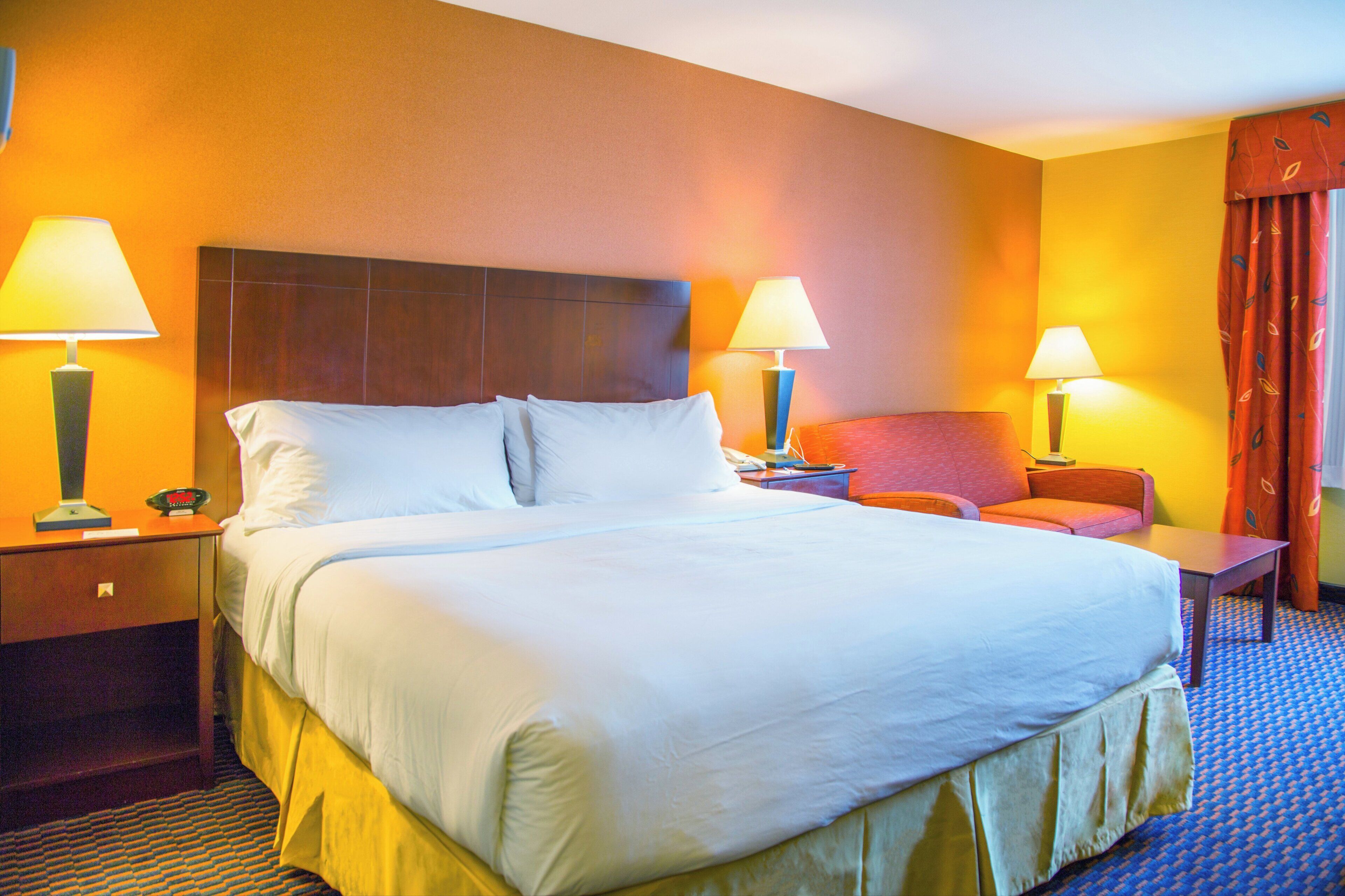 Une chambre d’hôtel avec un grand lit, deux tables de chevet avec des lampes, une chaise et un bureau avec un téléphone.
