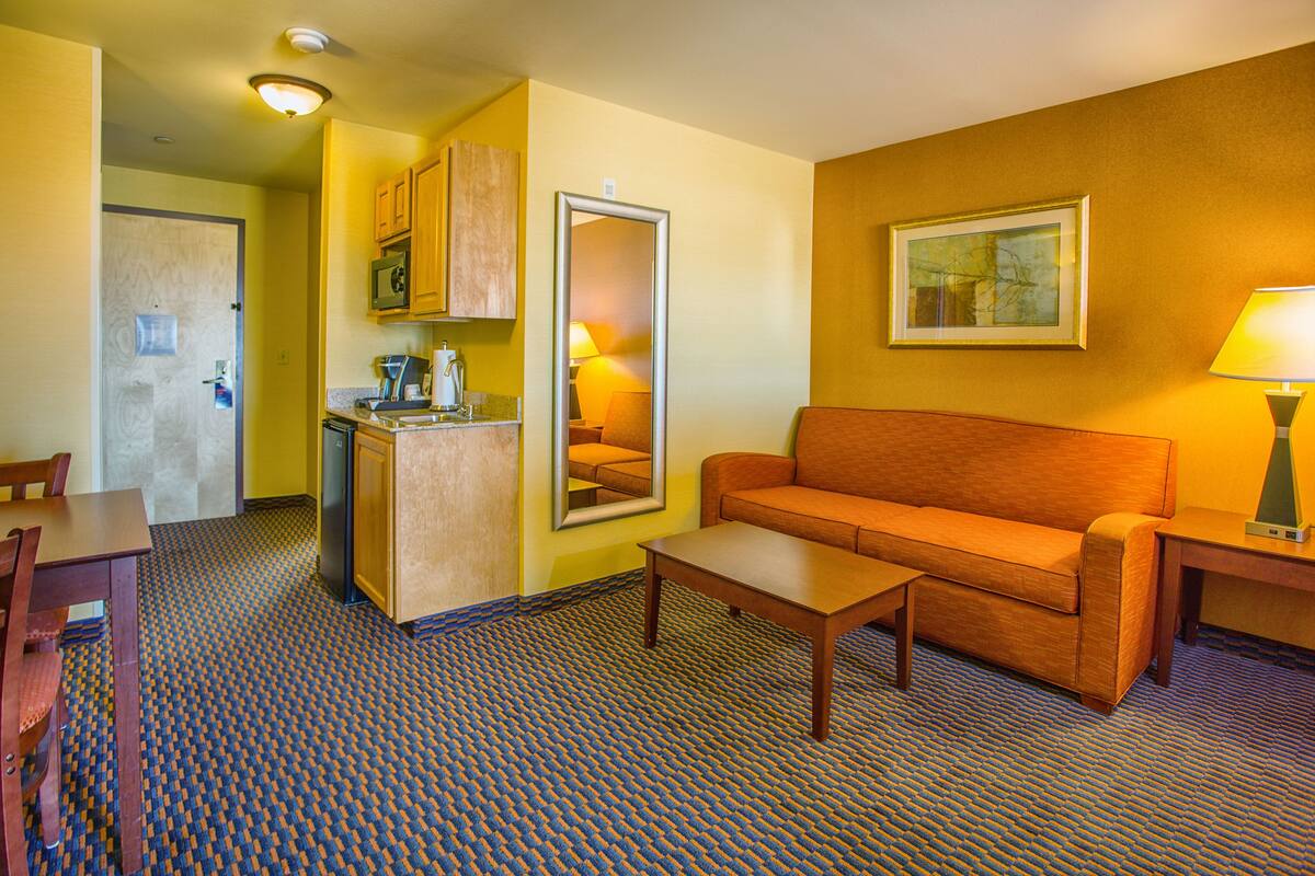 Una habitación de hotel compacta con kitchenette, un sofá, una mesa de centro y una mesa de comedor.
