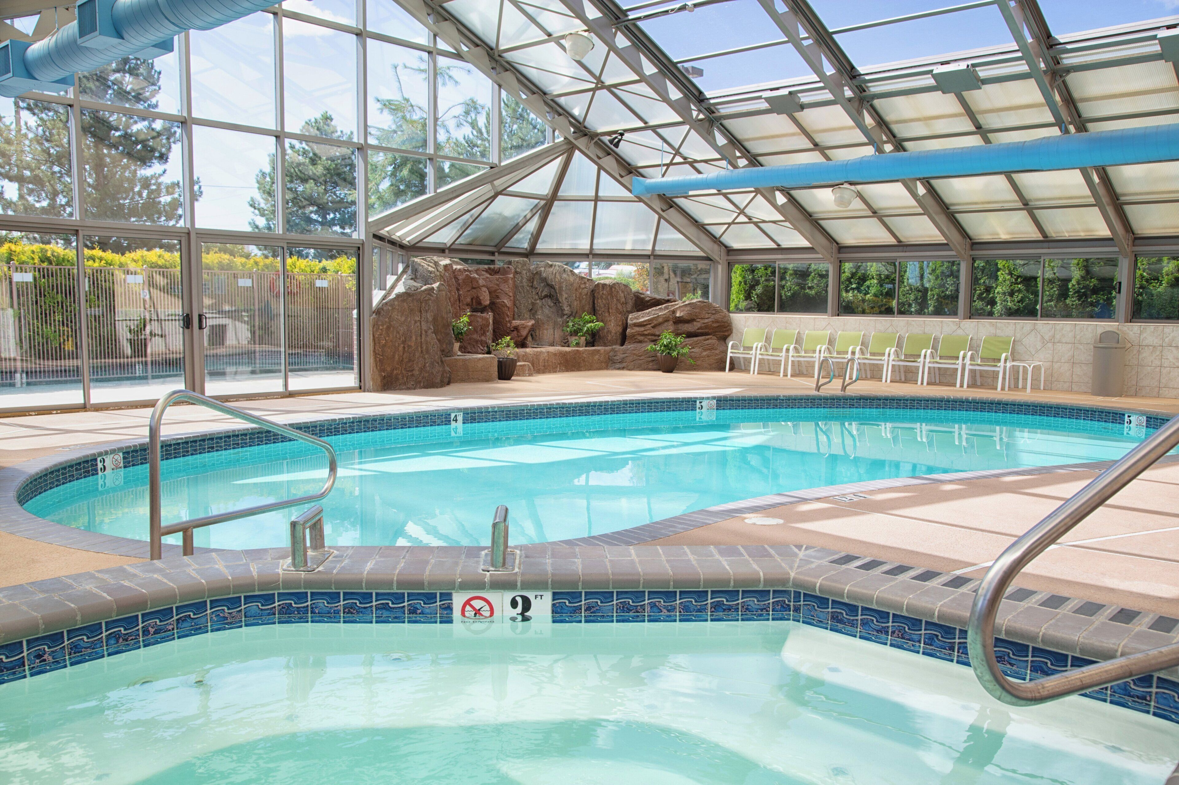 Una piscina interior con techo de cristal, una formación rocosa y zona de estar.