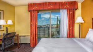 A hotel room with a large bed, a desk with two lamps, a chair, and a view of a building through a glass door. - Holiday Inn Express & Suites Richland by IHG (Richland)