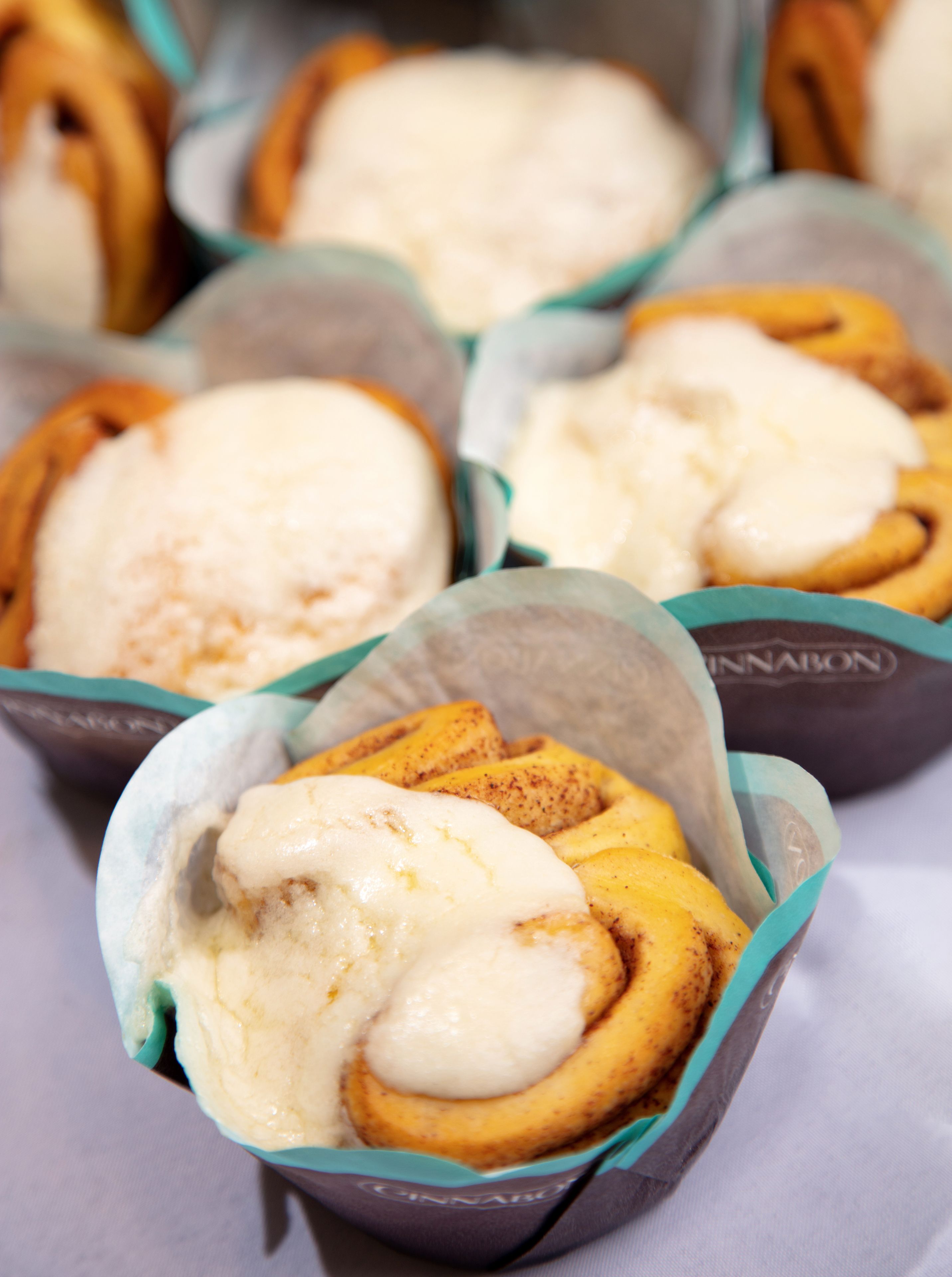 A close-up of cinnamon rolls with icing, in paper liners, on a table.
