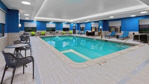 Una piscina interior con sillones reclinables y mesas, rodeada de paredes azules e iluminación empotrada.