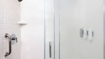 A shower area with white tiled walls, a glass door, a handheld showerhead, and a grab bar.