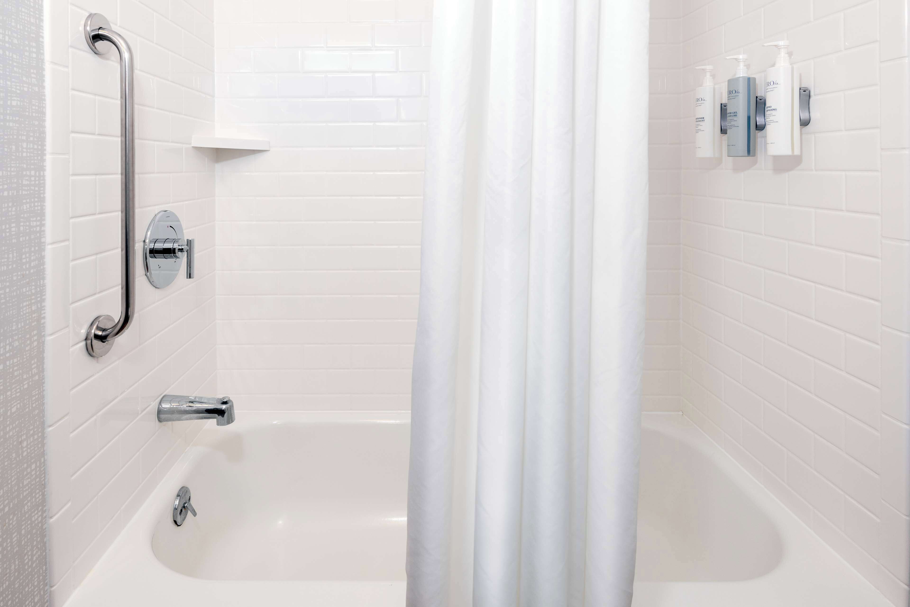 Une salle de bain blanche avec une baignoire, une douche équipée d’une barre d’appui et des articles de toilette fixés au mur.