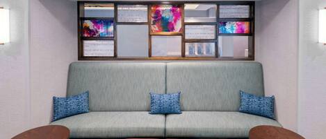 Een moderne hotellobby met een grijze bank, twee rode poefs en twee houten bijzettafels.