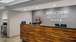 Un mostrador de recepción con un cartel que dice 'Welcome to the Ocean State', un diseño de paneles de madera y el logotipo de 'Hilton Honors'.