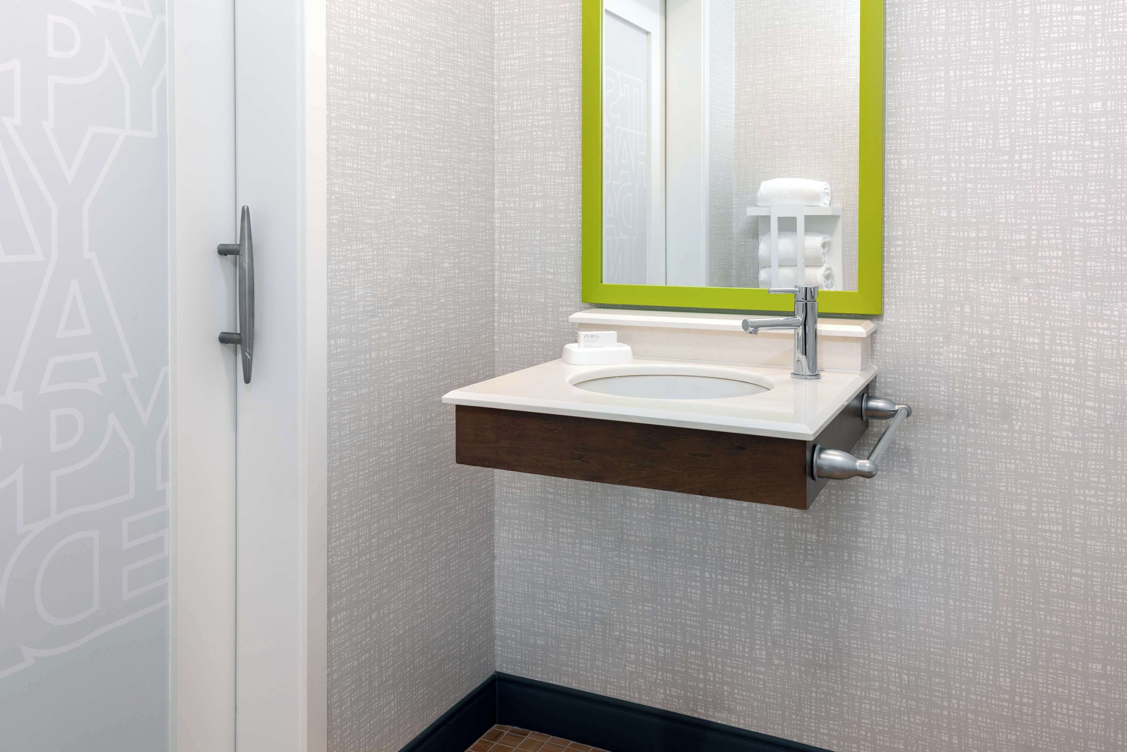 Un baño con lavamanos blanco, espejo con marco verde y un perchero para toallas.