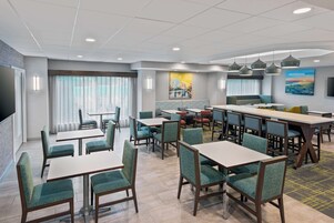 A modern dining area with tables and chairs, large windows with curtains, and artwork on the walls.