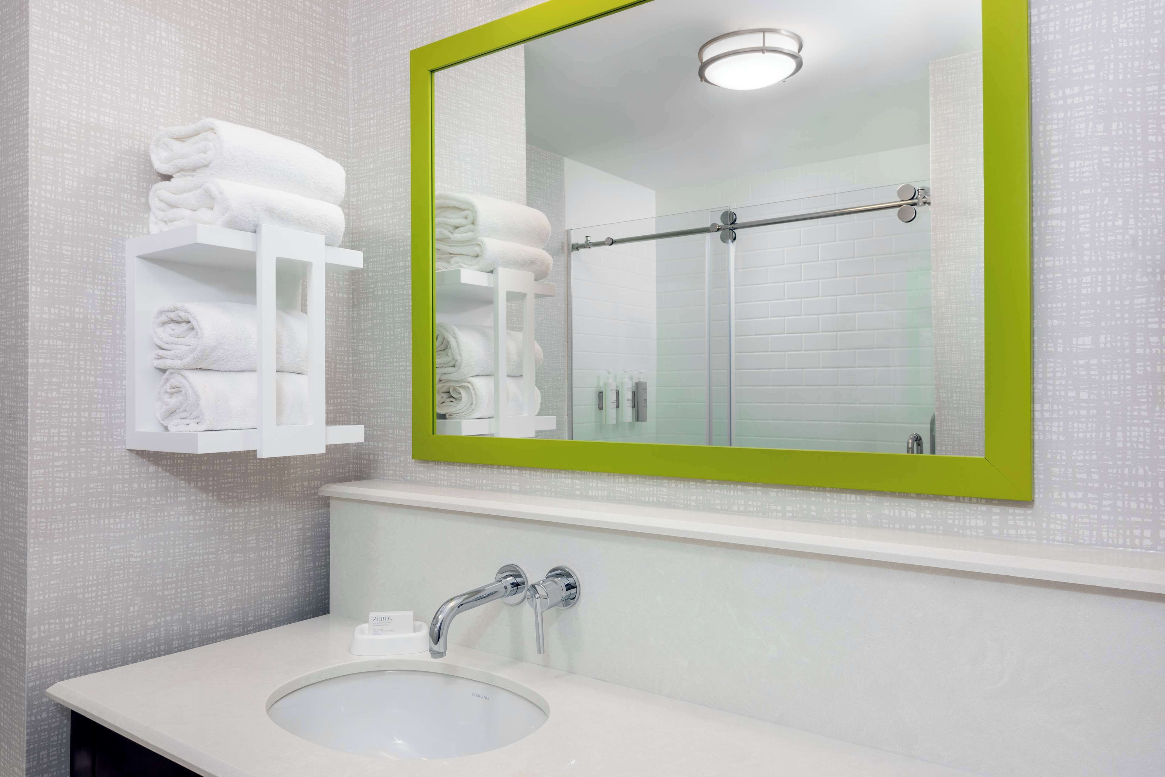 A bathroom with a white sink, a mirror with a green frame, and a towel rack with folded towels.