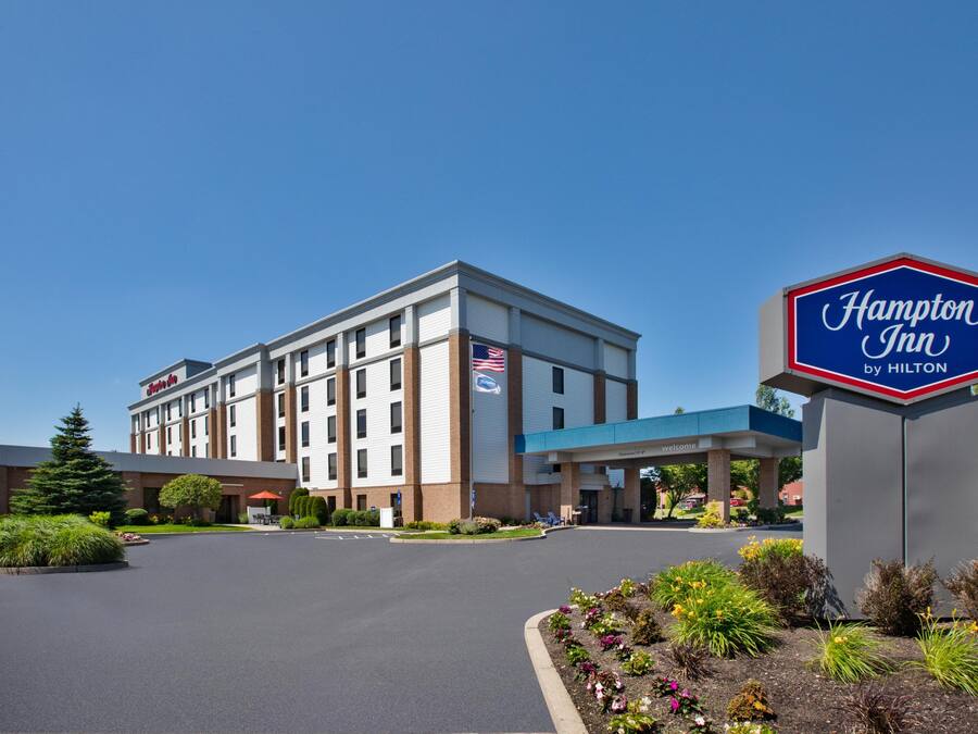 A Hampton Inn by Hilton hotel with a clear sky, a parking lot, and landscaped gardens.