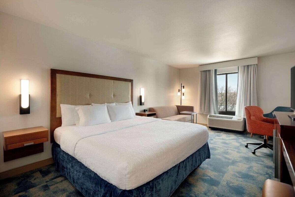 A hotel room with a large bed, bedside tables, a desk, a chair, and a window with curtains.