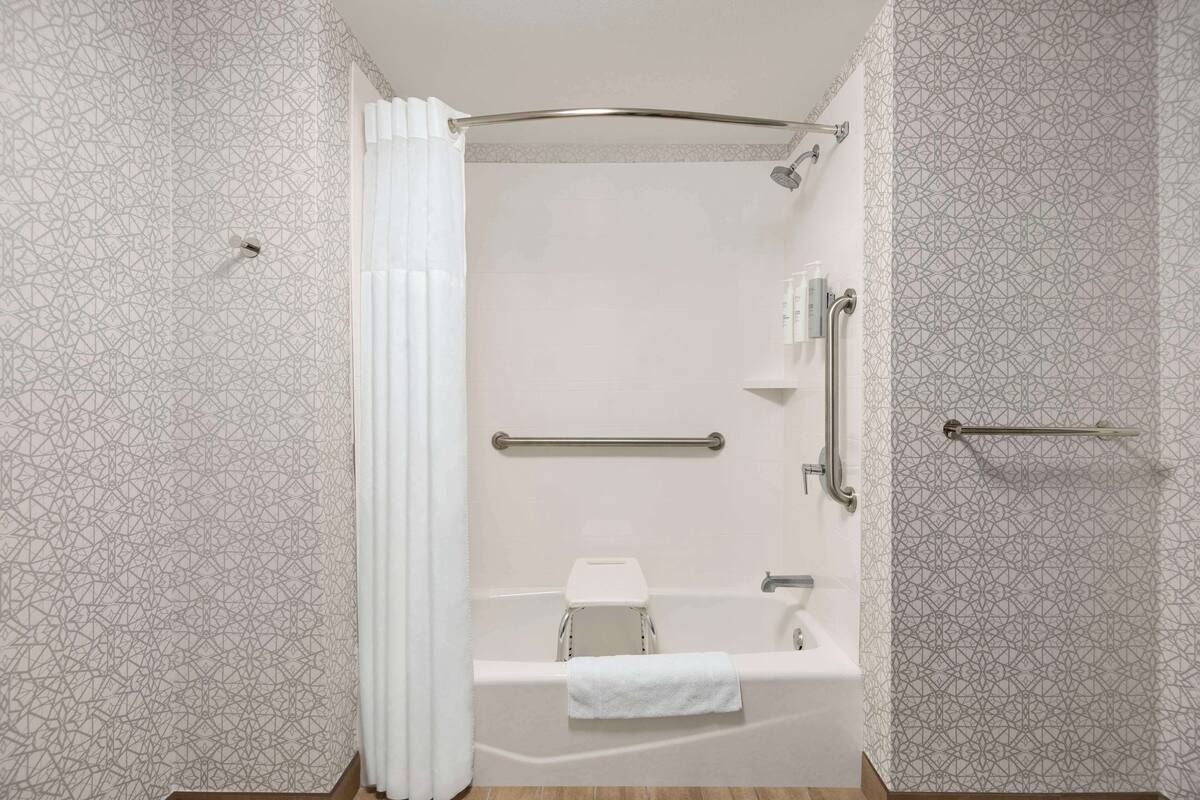 A modern bathroom with a shower, a toilet, and a handrail.