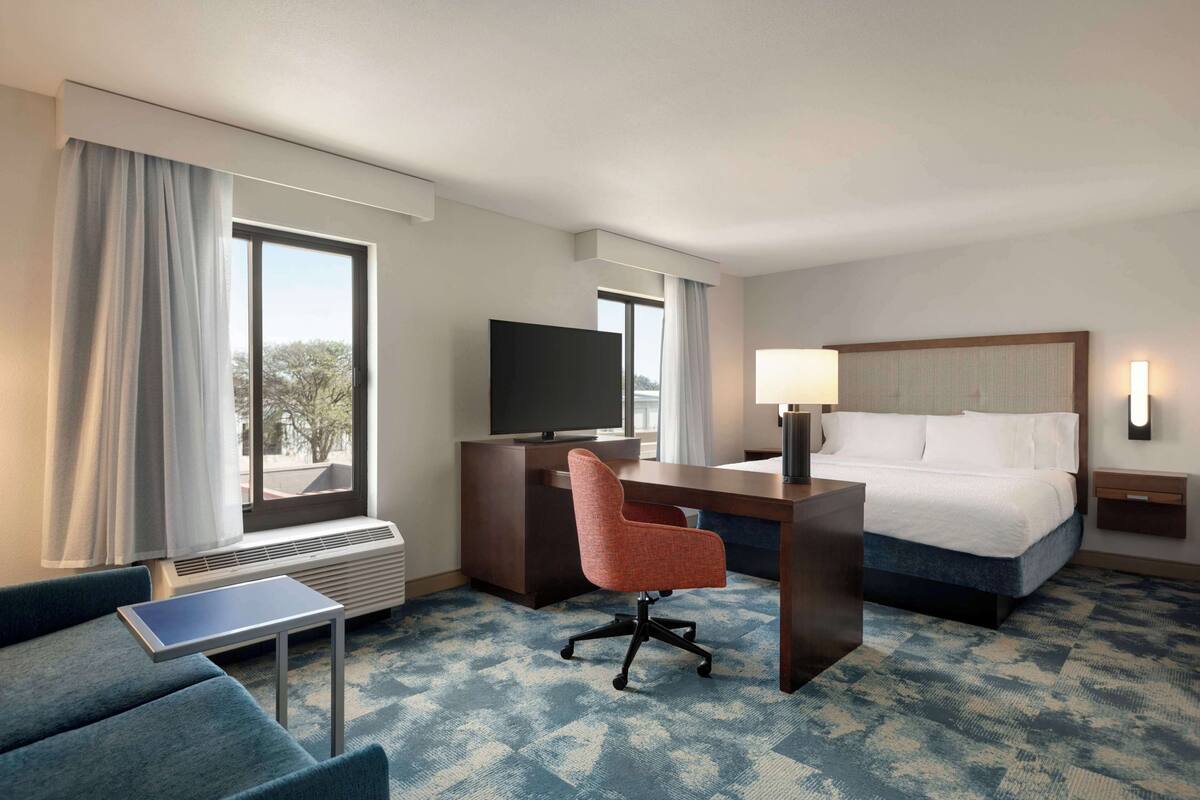 A hotel room with a bed, desk, chair, television, and a view of the outdoors.