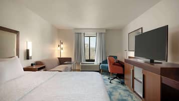 Una habitació d'hotel amb un llit gran, una taula de treball amb televisió de pantalla plana, una cadira, un sofà i una finestra amb cortines.