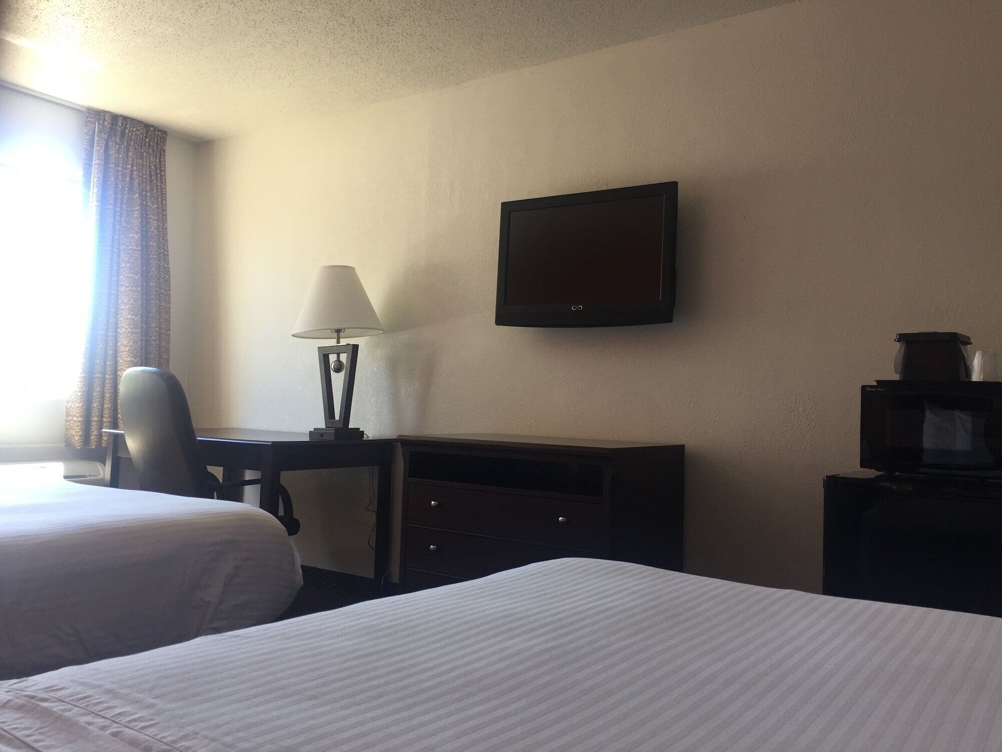 A hotel room with two beds, a desk with a lamp, a television, and a dresser.