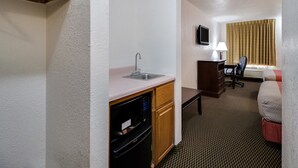 A compact hotel room with a kitchenette, a single bed, a desk with a chair, a TV, and a window with curtains. - Motel 6 Marion, IL (Marion)