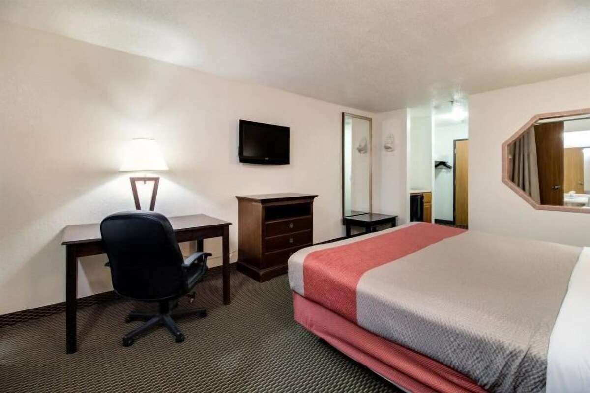 A hotel room with a bed, desk, chair, dresser, and a TV mounted on the wall.