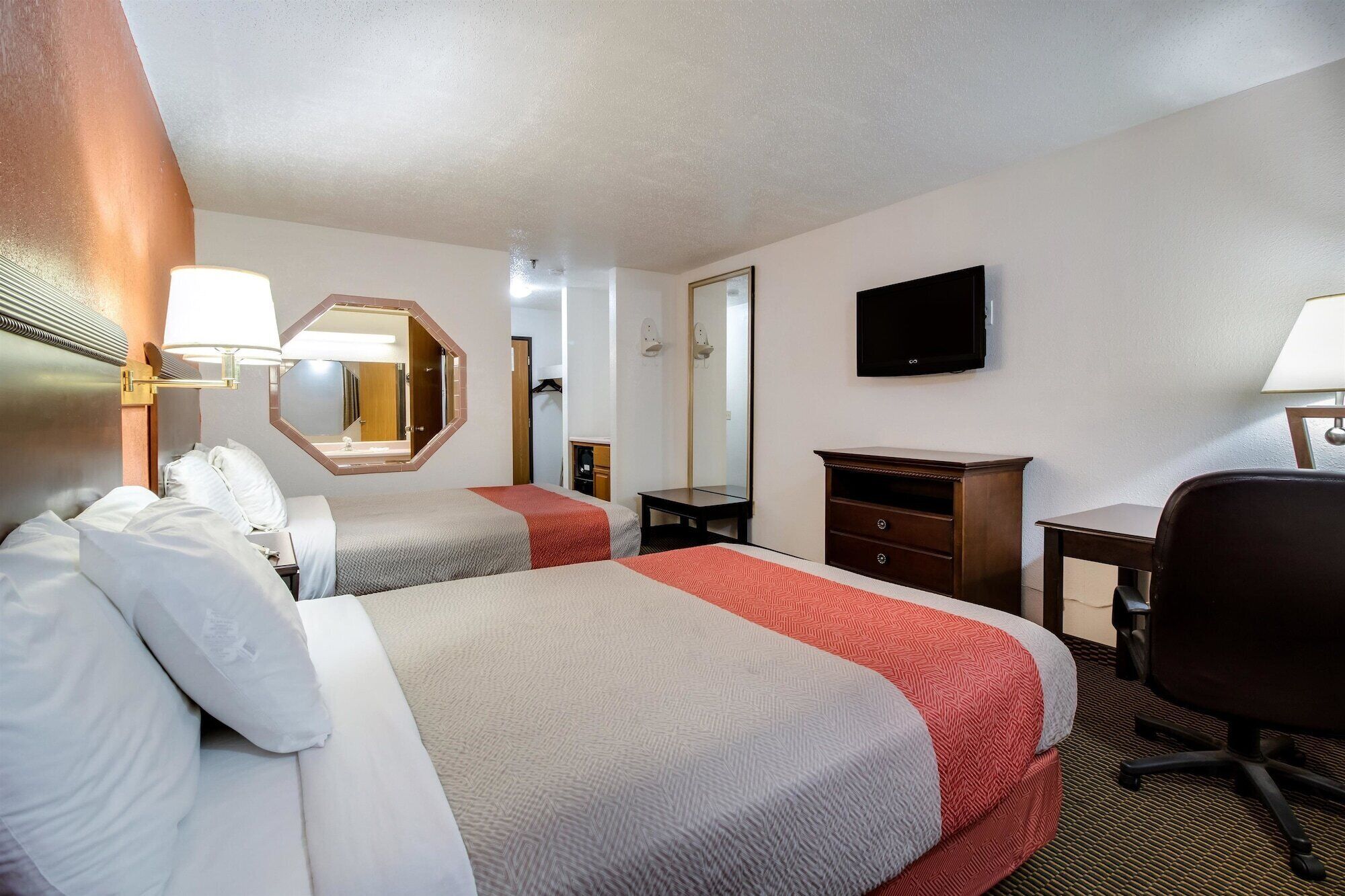 A hotel room with two beds, a desk, a chair, a TV, and a mirror.