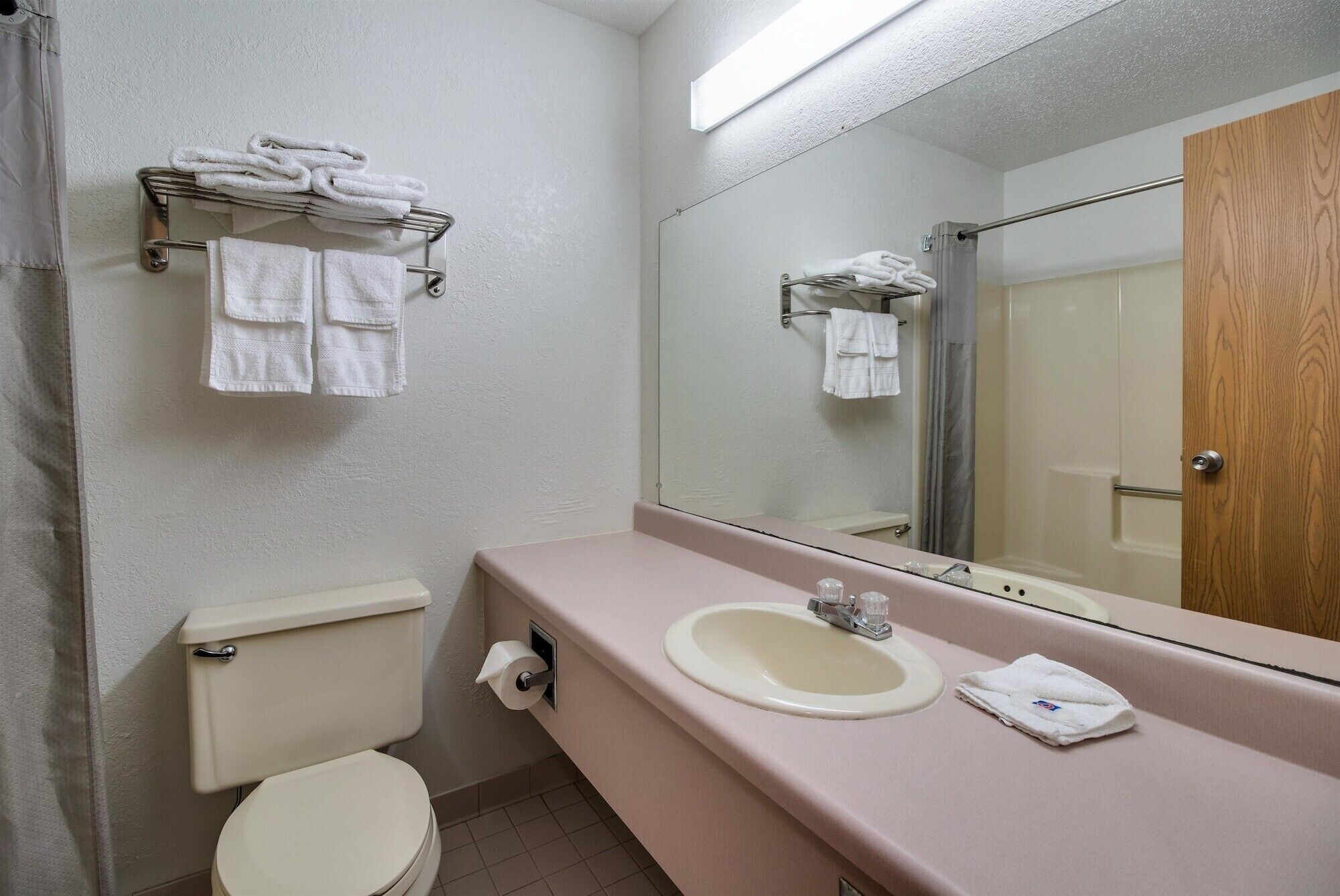 A bathroom with a toilet, sink, and mirror. There are towels on a rack and a shower curtain.