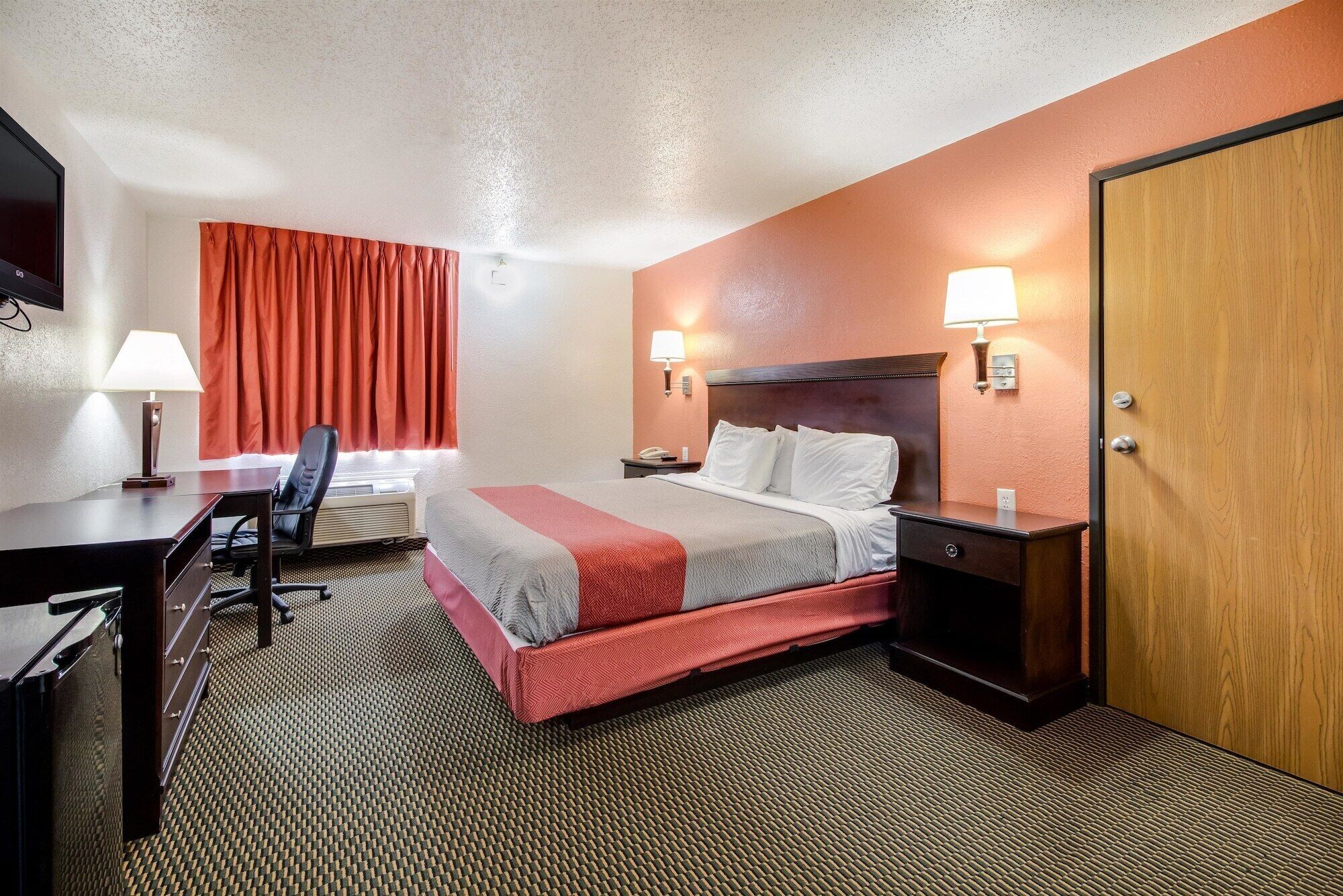 Une chambre d’hôtel avec un lit, un bureau, une chaise et une porte.