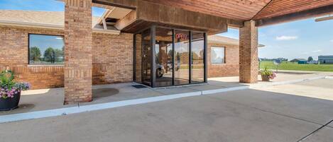 A building with a brick facade, a covered entrance with glass doors, and a clear sky.