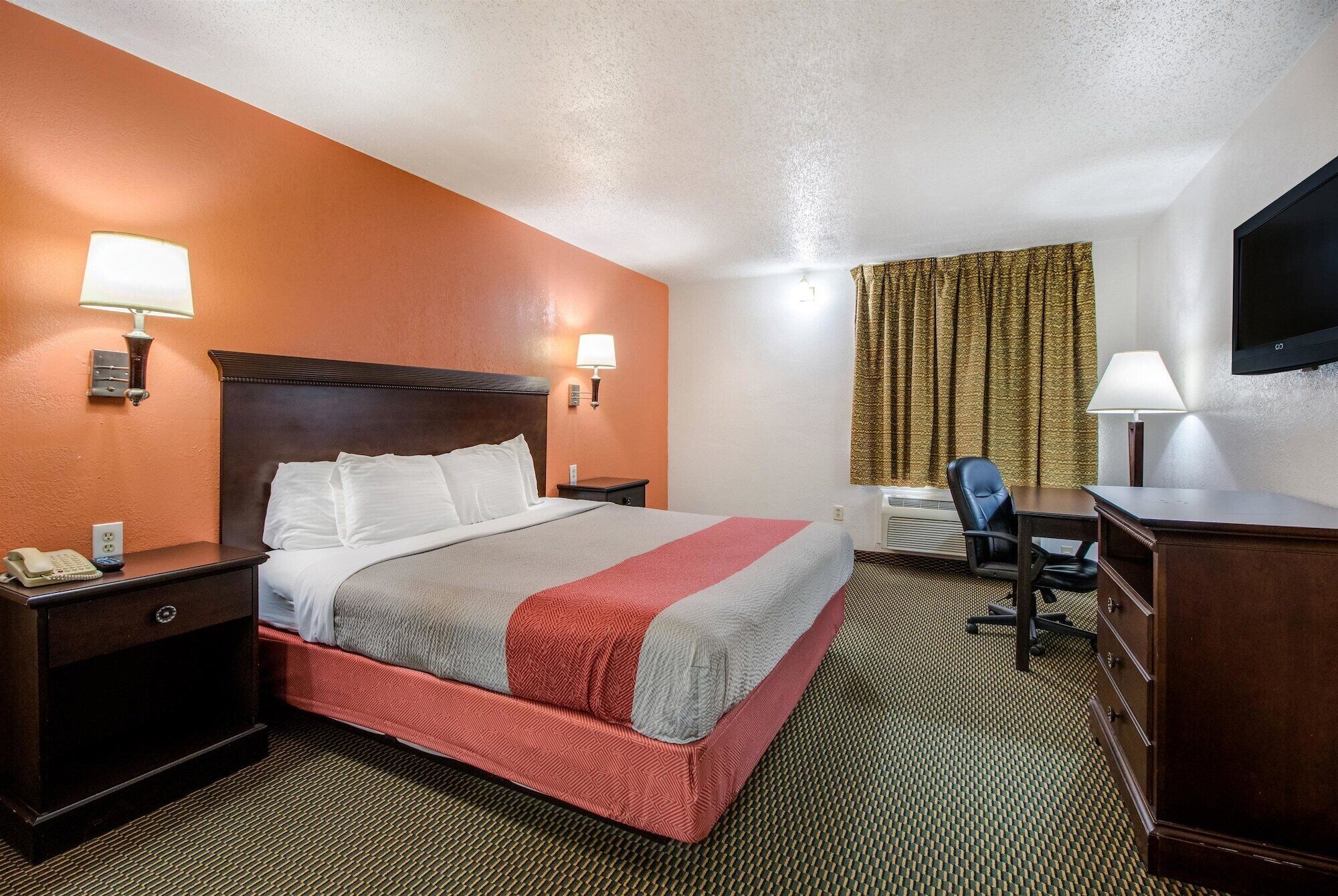 Una habitación de hotel con cama, lámparas de noche, un escritorio con silla, teléfono y televisor.